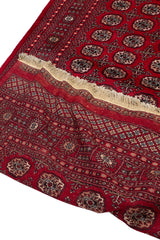 Alfombra rectangular roja con patrón repetitivo de formas ovaladas en tonos oscuros y borde decorado.