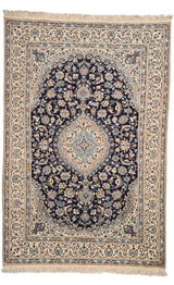 Vista completa de la alfombra clásica con medallón central en tonos marfil y azul sobre un fondo oscuro, rodeada por una guarda floral clara.