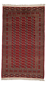 Vista completa de la alfombra oriental con fondo rojo oscuro y patrón repetido de motivos geométricos en azul, beige y naranja.