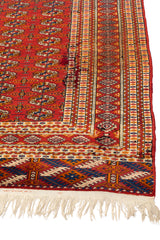 Vista diagonal destacando la textura y los bordes ornamentales de la alfombra en tonos rojo, azul y beige.