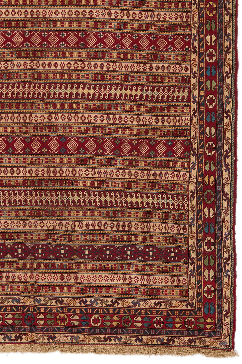 Detalle del extremo inferior derecho de la alfombra, mostrando el borde decorativo y los motivos geométricos y florales en colores vivos.