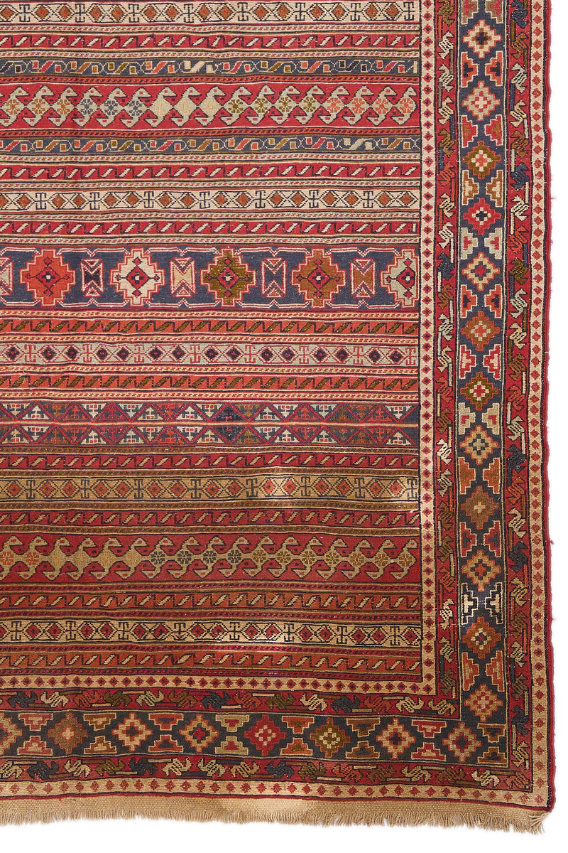 Detalle inferior derecho de la alfombra, mostrando motivos tribales en colores rojo, azul y beige.