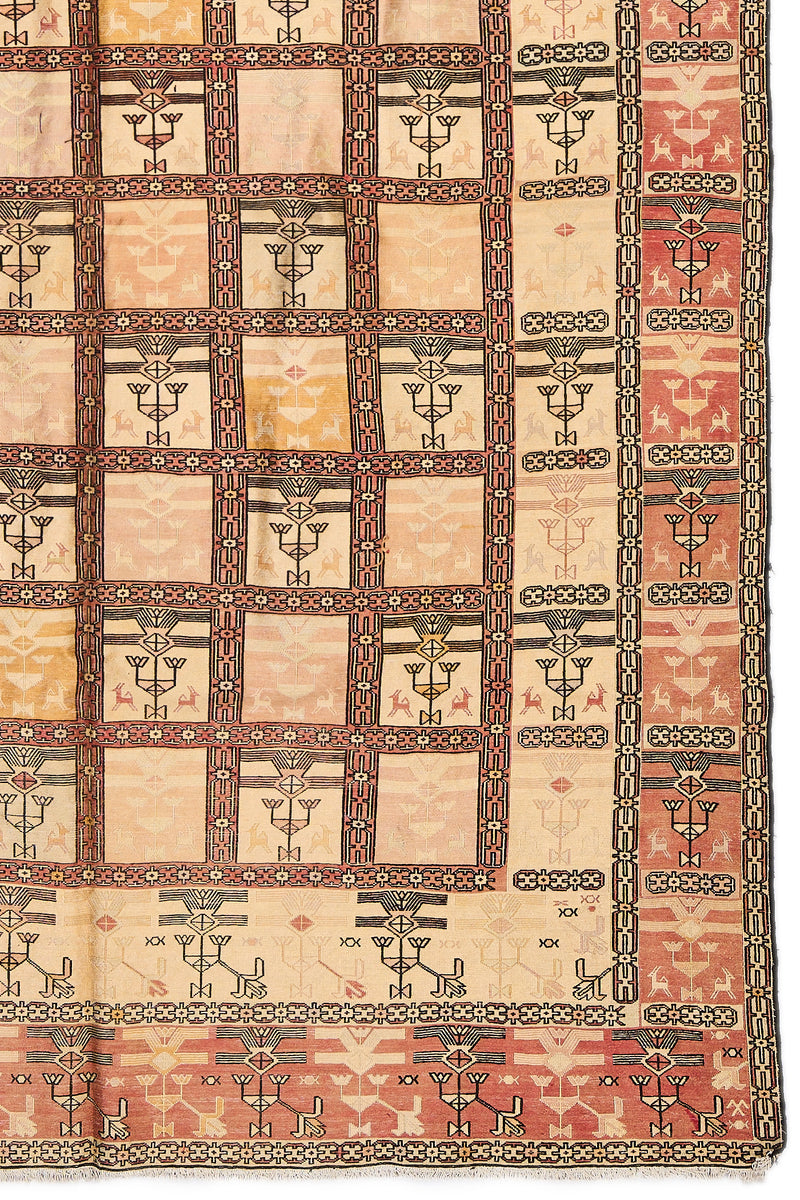 Detalle del extremo inferior derecho de la alfombra, mostrando los motivos geométricos y colores desgastados en beige y rosado.