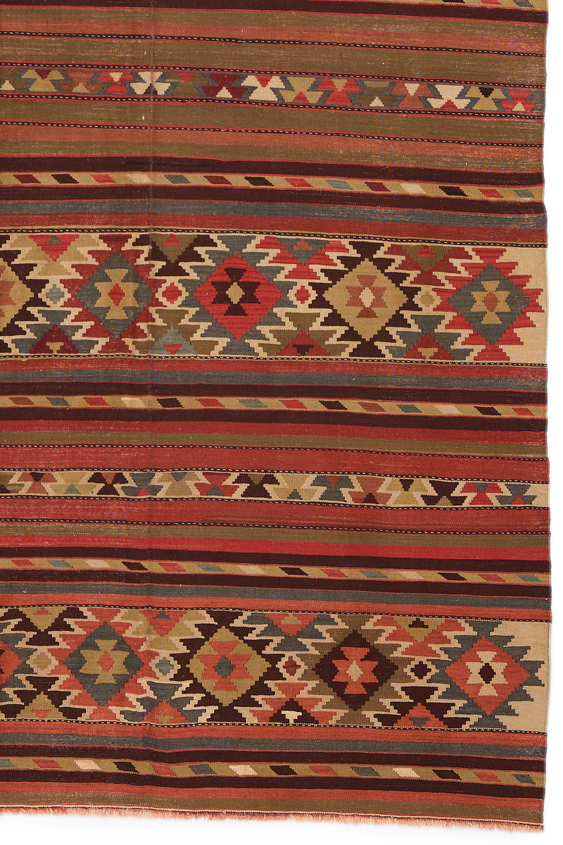Detalle del extremo inferior de la alfombra kilim, mostrando la repetición de figuras en rombos multicolores y franjas de colores tierra.