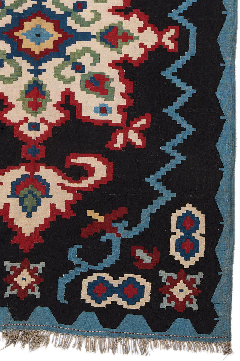 Detalle inferior derecho de la alfombra mostrando la precisión del tejido en los motivos florales y las figuras estilizadas en azul, blanco y rojo.