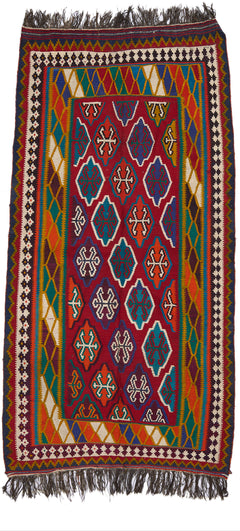 Vista completa de una alfombra artesanal con fondo rojo intenso, decorada con medallones geométricos y múltiples franjas coloridas en el borde.