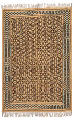 Vista completa de una alfombra artesanal de fondo beige con patrones geométricos marrones, enmarcada por una guarda de rombos celeste y negro.