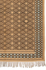 Detalle de la esquina inferior derecha de la alfombra, mostrando el diseño geométrico en diamantes y el borde celeste con flecos beige.