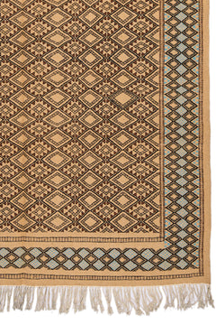 Detalle de la esquina inferior derecha de la alfombra, mostrando el diseño geométrico en diamantes y el borde celeste con flecos beige.