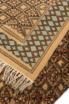Detalle de la parte trasera de la alfombra doblada, mostrando el reverso del diseño artesanal y los flecos de lana.