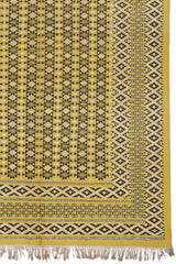 Detalle del lado inferior derecho de la alfombra mostrando el intrincado patrón de diamantes negros sobre fondo mostaza.
