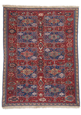 Vista completa de alfombra oriental con fondo rojo y motivos geométricos en azul, rosa y beige.