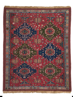 Vista completa de una alfombra kilim tradicional con fondo rojo intenso y motivos geométricos en azul y verde.