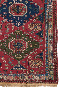 Detalle lateral de la alfombra mostrando el borde decorado en tonos azul y rojo con patrones simétricos.