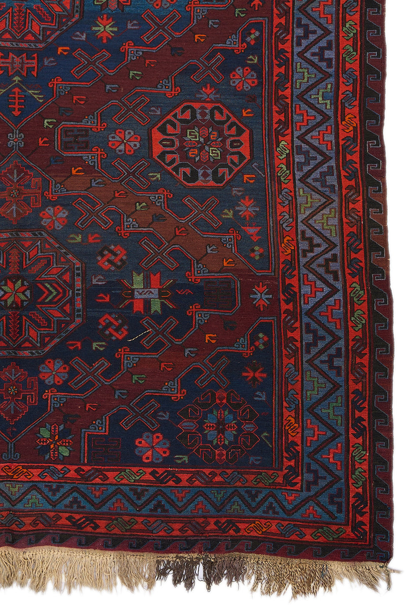 Detalle lateral derecho de alfombra kilim con bordes en zigzag multicolor y motivos florales enmarcados por figuras geométricas.