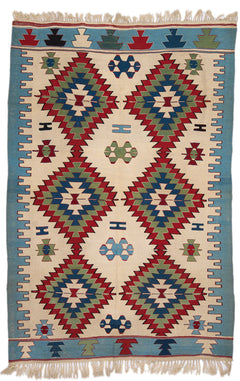 Vista completa de una alfombra kilim de fondo beige con grandes motivos geométricos en forma de diamante, en tonos rojo, verde y azul.