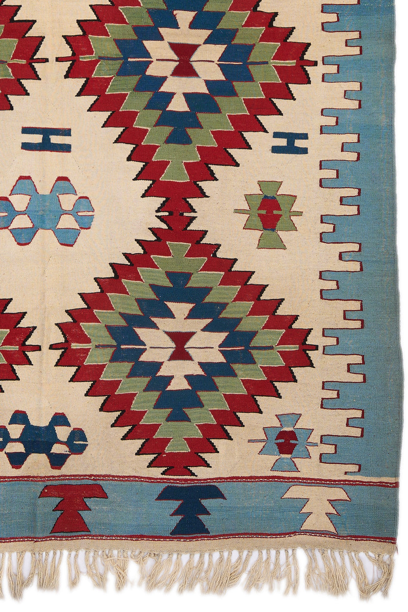 Detalle lateral inferior derecho de la alfombra, mostrando los patrones en zigzag en azul, verde y los bordes decorativos en rojo.