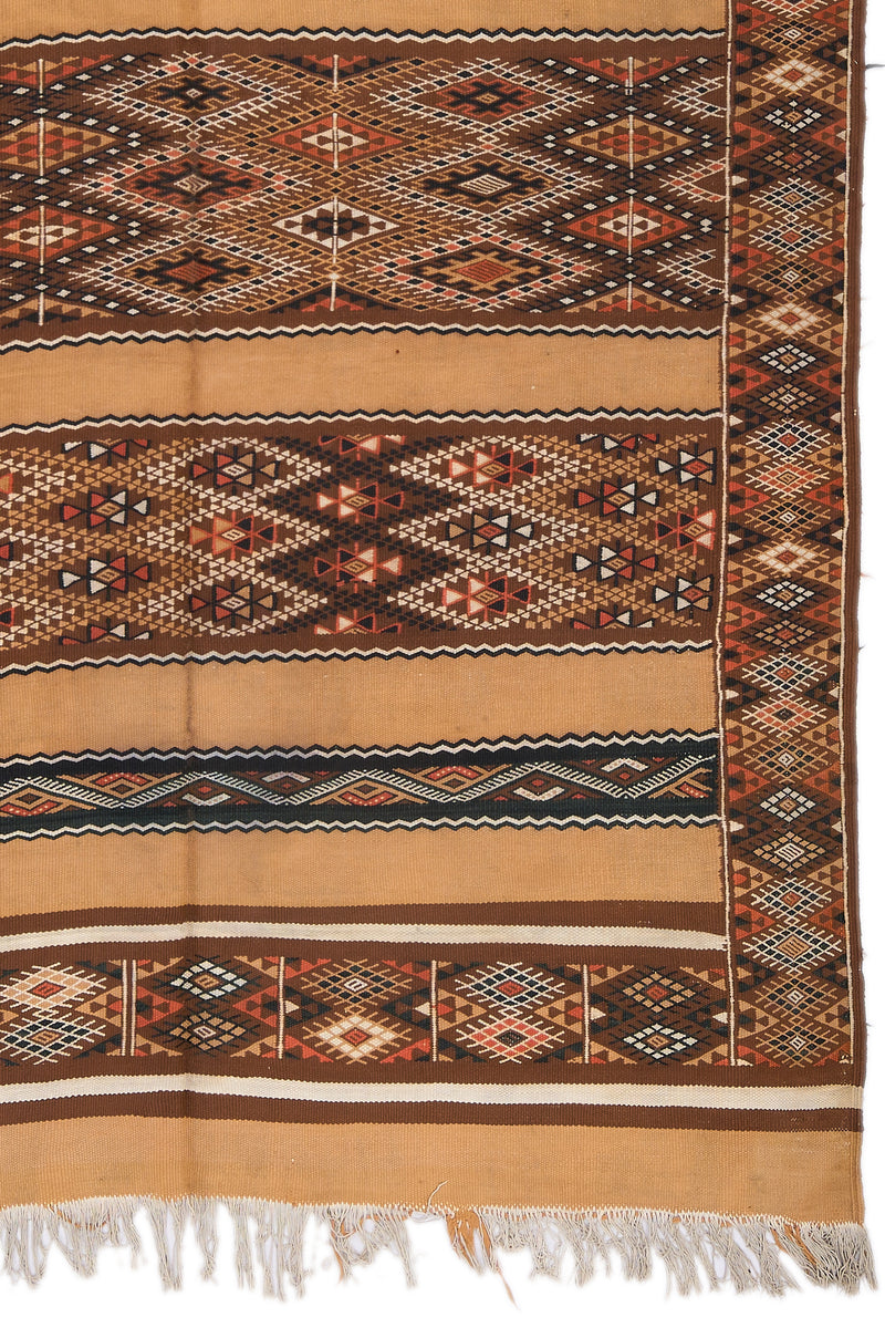 Detalle de los motivos geométricos centrales y bordes laterales de la alfombra kilim en colores marrón, negro, beige y blanco.
