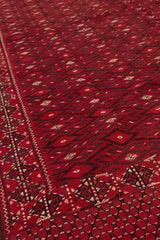 Toma en perspectiva lateral de la alfombra kilim roja, resaltando la textura tejida y la repetición de motivos geométricos.