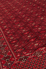 Vista en ángulo bajo de la alfombra kilim roja, enfocando el diseño en zigzag y la simetría de los rombos alineados.