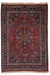 Vista completa de la alfombra de fondo rojo intenso, decorada con un medallón central simétrico y bordes oscuros con motivos florales en azul, beige y rosa.