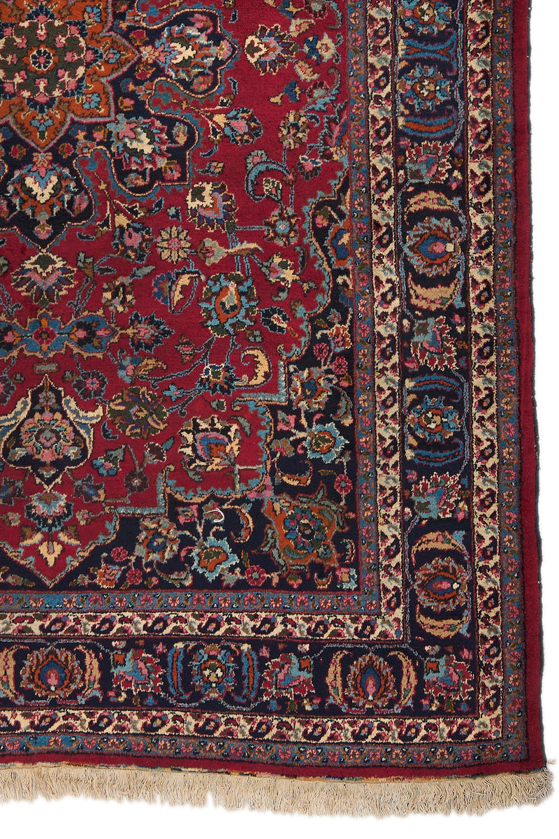 Detalle del borde inferior derecho de la alfombra mostrando patrones florales en azul, beige, naranja y rosado sobre fondo negro.