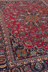 Toma lateral cercana de la alfombra donde se observan flores con tonos azul, verde oliva, rojo vino y bordes en beige sobre fondo negro