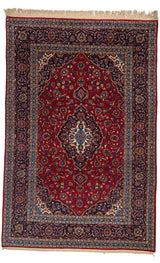 Vista completa de alfombra persa con fondo rojo , medallón central marfil y bordes azul marino con intrincados motivos florales.