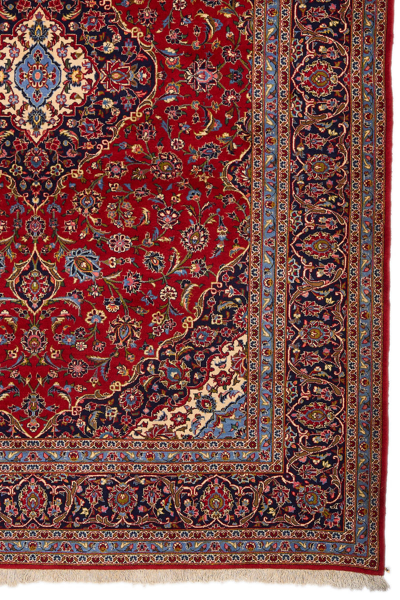 Detalle del borde derecho de la alfombra persa, mostrando el marco con motivos florales sobre fondo azul marino y celeste.