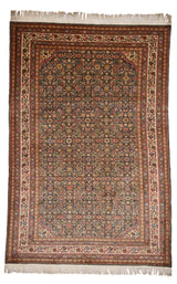 Vista superior completa de una alfombra persa con fondo verde oliva y detallado patrón floral en tonos rosado, morado, ocre y azul celeste, rodeada por una guarda color marfil decorada con motivos florales y geométricos.
