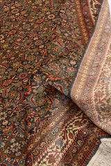 Toma artística con parte de la alfombra levantada mostrando el reverso del tejido y el diseño minucioso de flores y hojas multicolores sobre fondo oscuro.