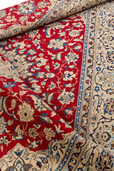 Detalle de esquina de la alfombra enrollada, mostrando el reverso y los nudos, con predominio de los colores rojo, marfil, beige y azul.