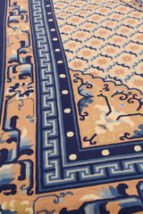 Vista en perspectiva del borde de la alfombra persa, mostrando franjas azul marino con detalles en marfil y diseño ondulado en tonos tierra.