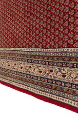 Vista en perspectiva del borde de la alfombra, destacando la textura y el diseño intrincado de la franja externa en beige, azul, verde oliva y rojo.