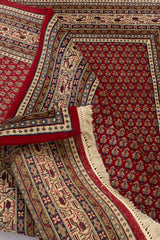 Imagen de la alfombra parcialmente doblada, donde se aprecian tanto el anverso como el reverso tejido con precisión artesanal y detalles en múltiples colores.