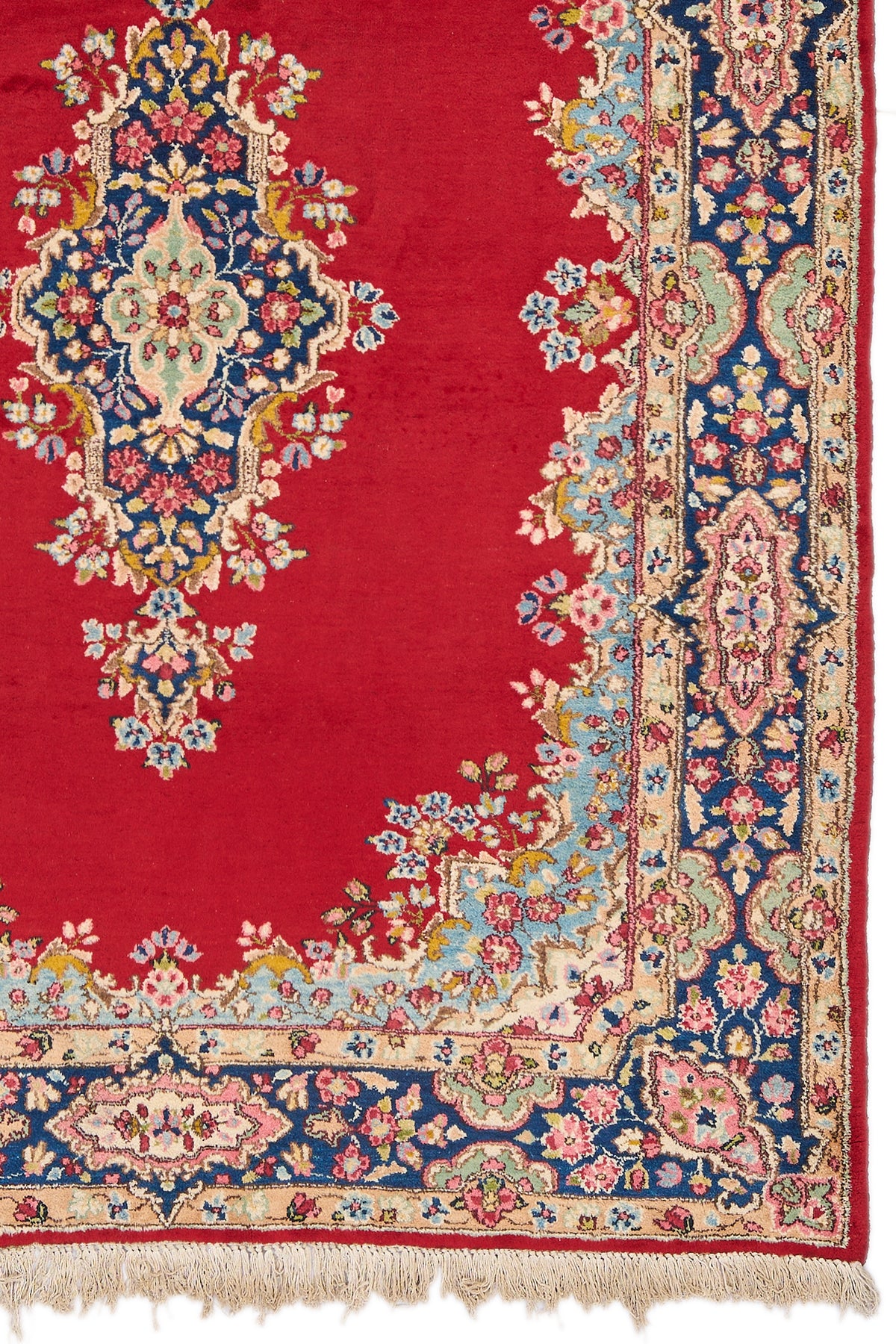 Detalle del medallón central y esquina derecha de la alfombra persa, con intrincados motivos florales sobre fondo rojo y borde azul marino decorado con flores rosadas.