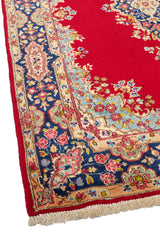 Esquina inferior derecha de la alfombra persa, destacando la riqueza de colores y los detalles florales del marco decorativo sobre fondo azul y beige.