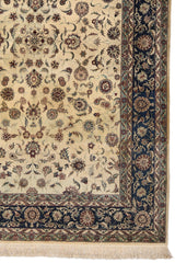 Detalle del borde derecho de la alfombra persa, mostrando flores entrelazadas en tonos vino, beige, azul y verde sobre fondo azul marino.