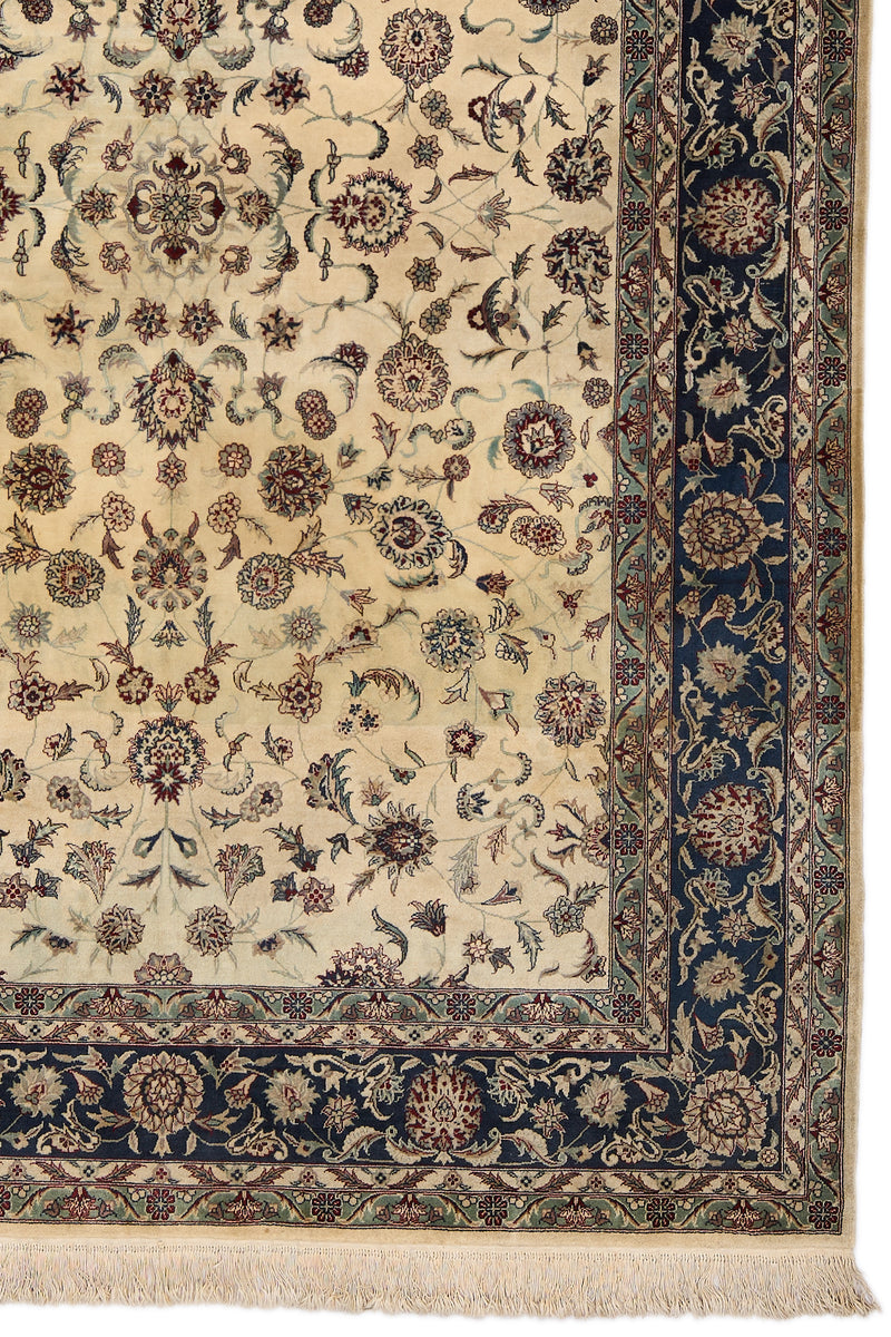 Detalle del borde derecho de la alfombra persa, mostrando flores entrelazadas en tonos vino, beige, azul y verde sobre fondo azul marino.