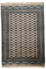 Vista completa de alfombra oriental con fondo beige y patrones geométricos repetitivos en celeste, dorado y negro.
