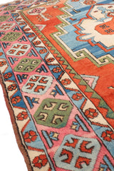 Vista lateral en perspectiva de la alfombra Kazak, destacando el relieve del tejido y los bordes ornamentados en rosa y verde.