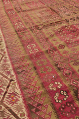 Vista angular de la alfombra kilim mostrando el patrón repetitivo en burdeos y los bordes con franjas y formas florales.