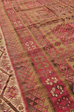 Vista angular de la alfombra kilim mostrando el patrón repetitivo en burdeos y los bordes con franjas y formas florales.