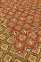 Vista lateral en ángulo de la alfombra kilim resaltando el patrón de estrellas escalonadas sobre fondo rojo y la textura plana del tejido.