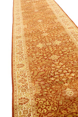 Vista lateral de alfombra tipo corredor mostrando el diseño floral simétrico en tonos ocre, dorado y terracota, enmarcado por una guarda clara