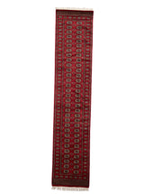 Vista completa de alfombra oriental larga con fondo rojo y diseño repetitivo en tonos oscuros.