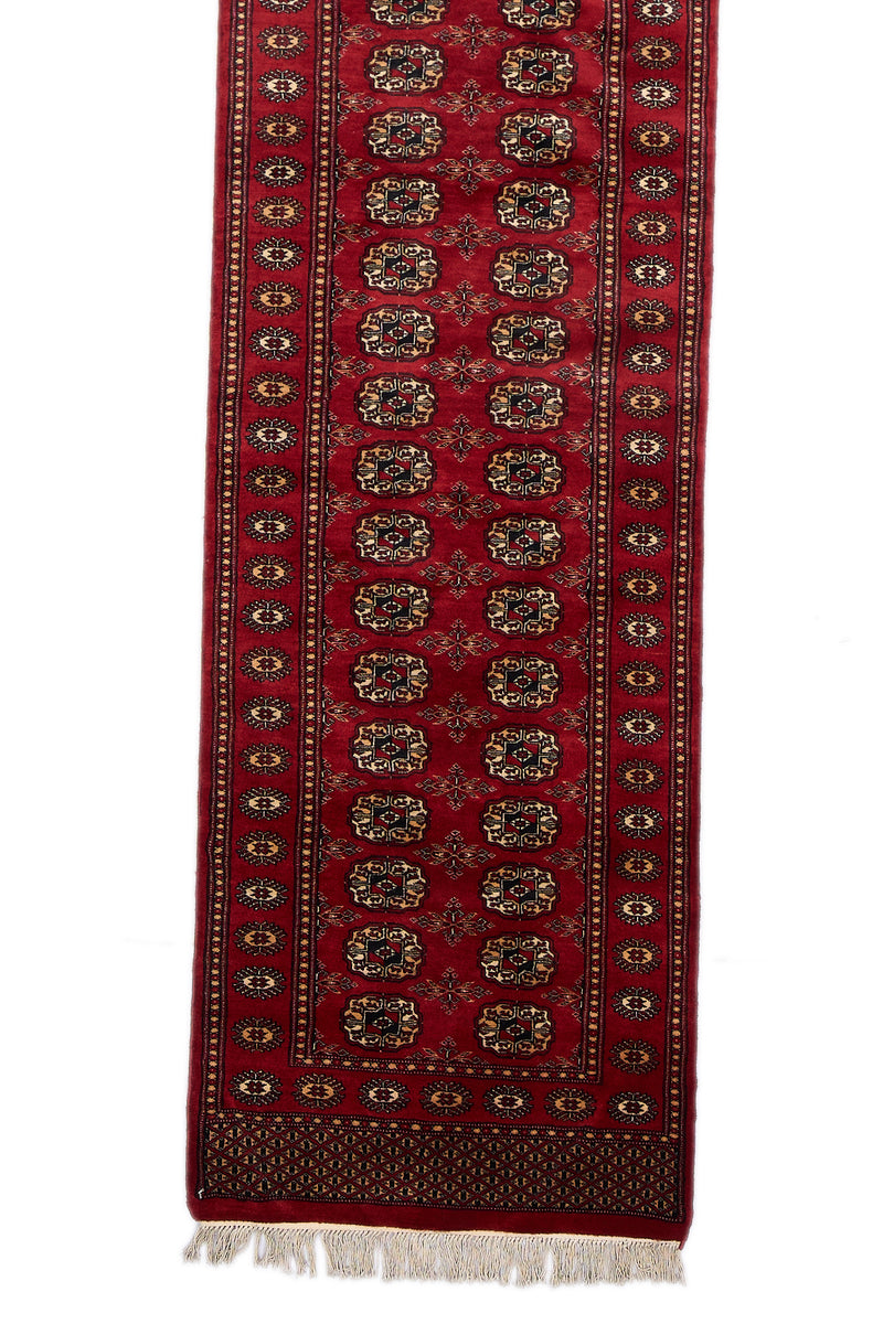 Detalle central de la alfombra con patrón geométrico repetido sobre fondo rojo.