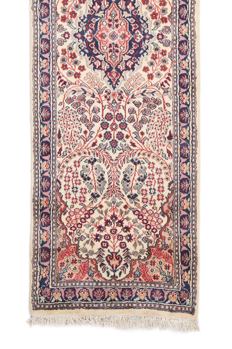 Detalle del extremo inferior de la alfombra mostrando flores simétricas y borde decorado en tonos azul marino y rosa.