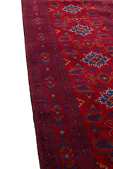 Perspectiva lateral de la alfombra resaltando el contraste entre el fondo rojo y los motivos azules.