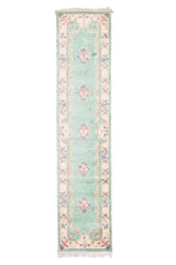 Alfombra de estilo floral vista completa en fondo verde pastel con motivos florales rosados y bordes decorativos beige.